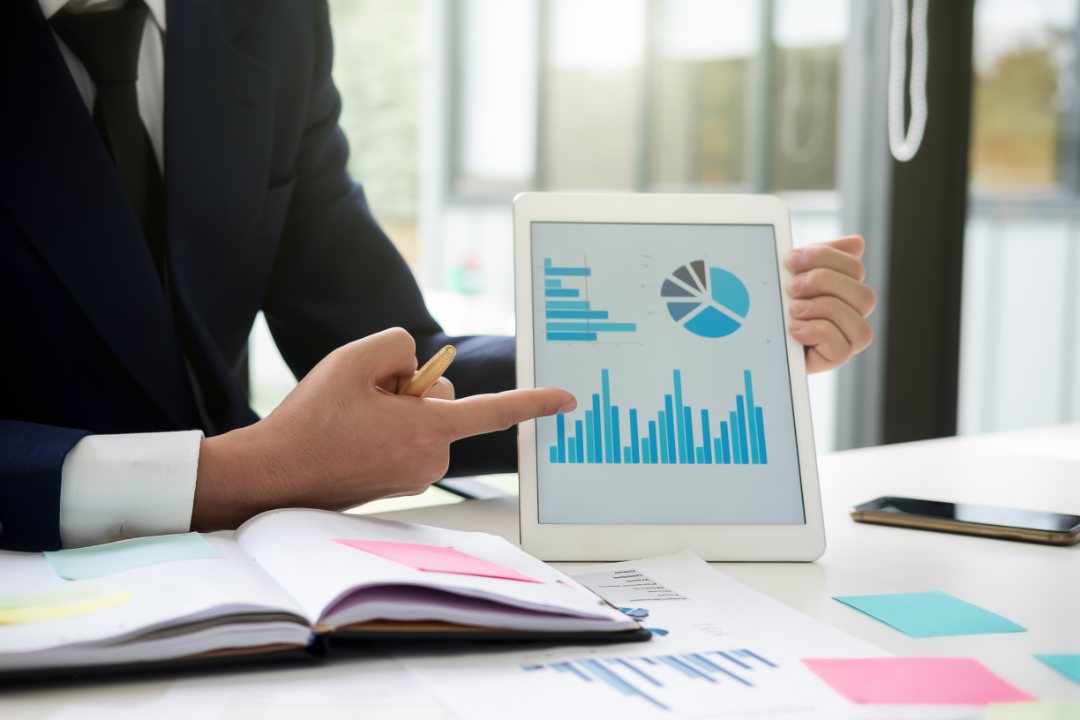 A digital marketer analyzing keyword rankings and search traffic trends on Ahrefs. The screen shows a keyword research dashboard with graphs and charts. A modern office setup with a mouse, keyboard, and coffee.