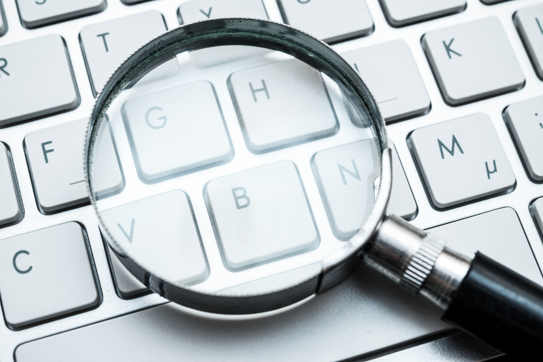 A stylized image of a magnifying glass positioned over a list of SEO keywords written on a document to suggest close keyword analysis.