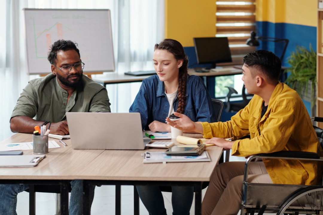 A team of marketers collaborating around a laptop with a large digital calendar on the screen.